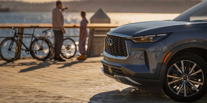 Front view of a gray Infiniti SUV on a pier, with blurred people and bicycles in the background.