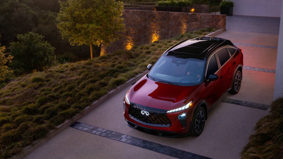 Red 2027 INFINITI QX65 with a black roof parked in a driveway at dusk