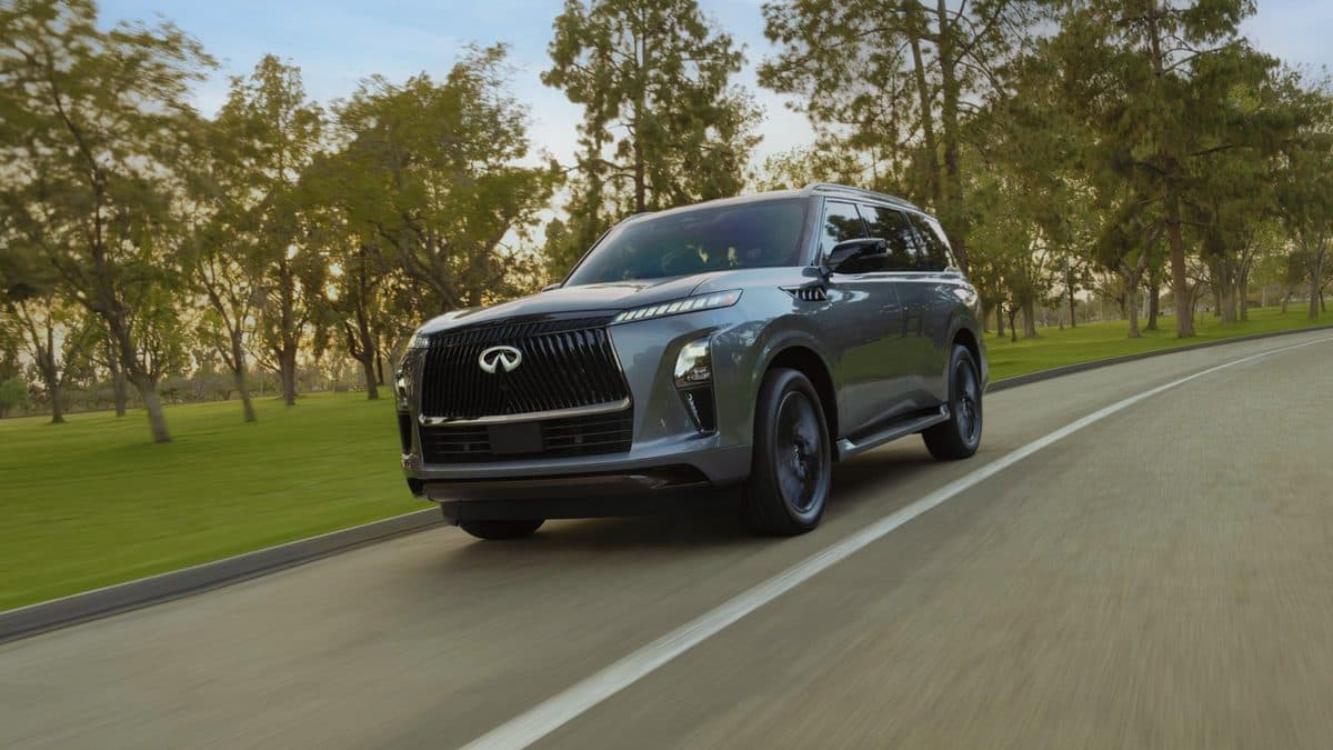 Gray 2027 INFINITI QX80 full-size luxury SUV driving on a tree-lined road