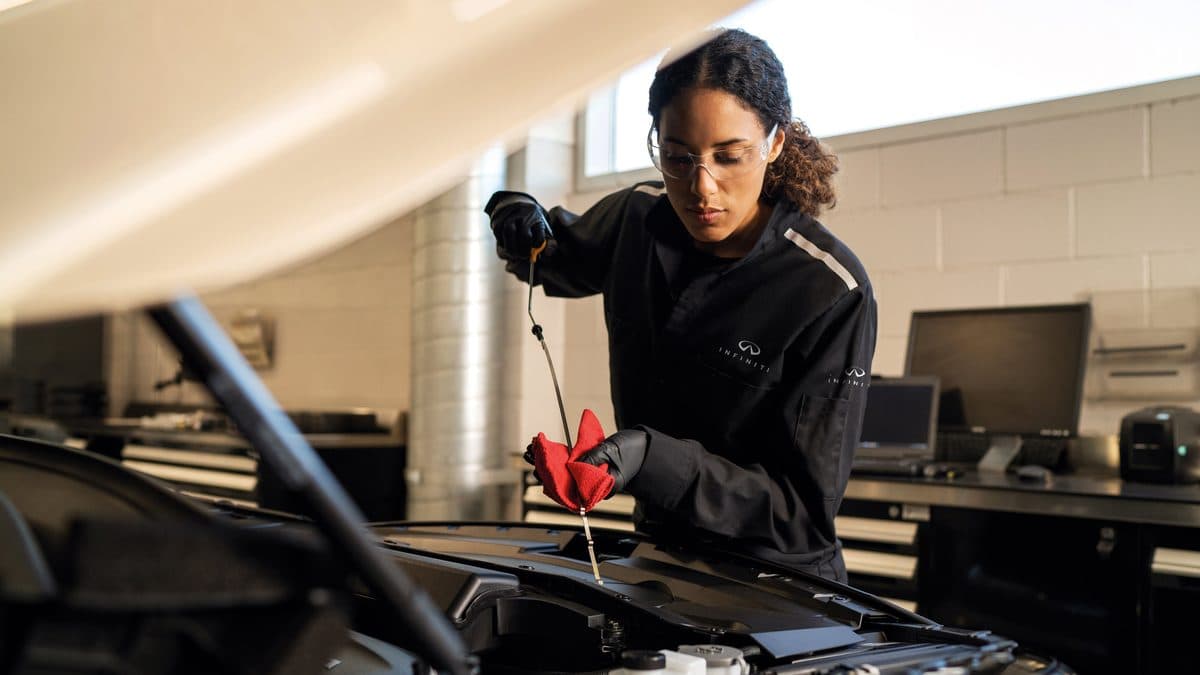 INFINITI service technician checking the engine oil level with a dipstick during scheduled maintenance