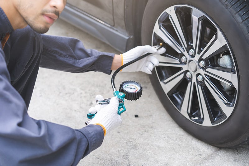 Mechanic checking and adjusting car tire pressure with an air gauge while wearing white gloves..